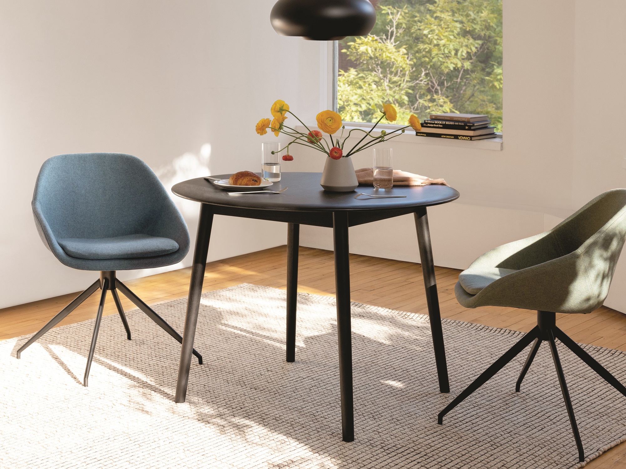 Blue dining chairs sit at a black round dinette set with pastry, water, and a vase of flowers