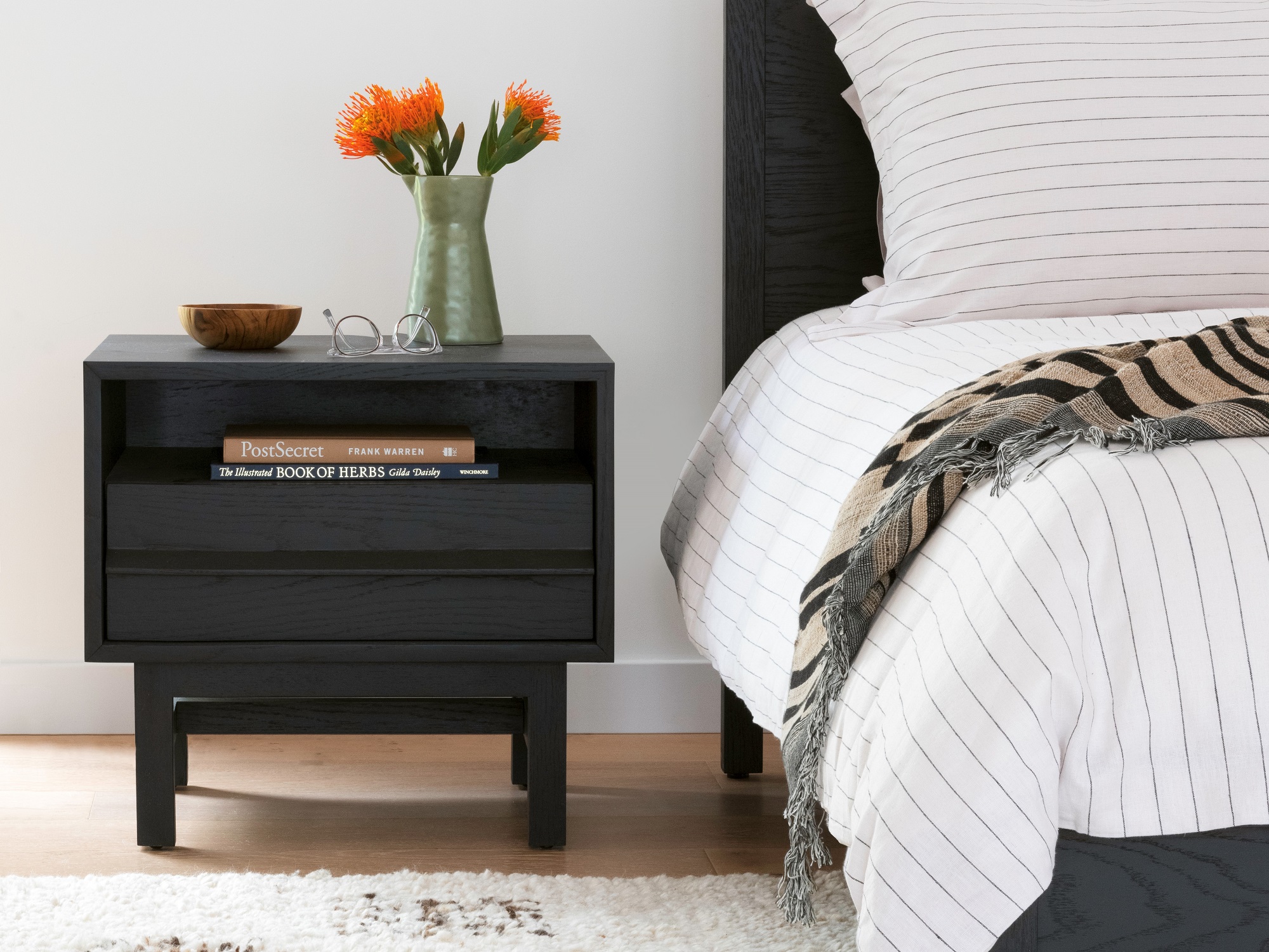Black oak nightstand with open shelf next to matching bed frame with white striped sheet set